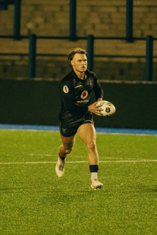A LooseHeadz player running with the ball under the floodlights